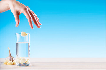 Hand throws garlic in a glass with water on a blue background, garlic water, disease prevention....