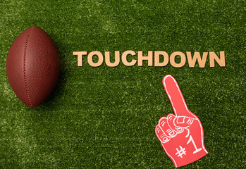 American football ball, foam finger and "Touchdown" made from wooden letters on green grass background