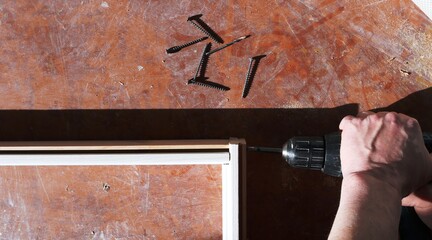 tightening screws into the base of the door frame body lying on the floor in the room being repaired, working with a screwdriver against a brown surface with several lying self-tapping screws