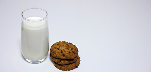 A glass of milk and three oat biscuits on a white background