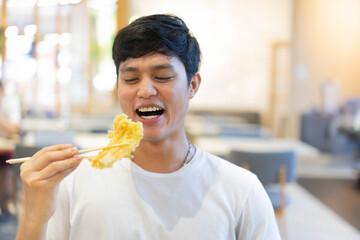 close up young cute asian japanese man smiling while using chopsticks to hold deeply fired of shrimp tempera at restaurant for asian eating culture tradition concept