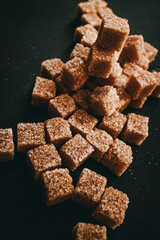 Brown cane sugar in cubes on a black background. Still life. Carbohydrates and non-diet food. Calories.