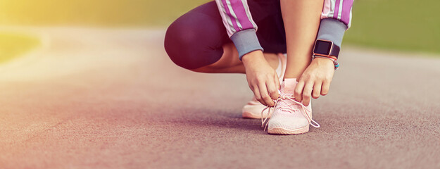 Modern active young woman tying shoelaces before running in park