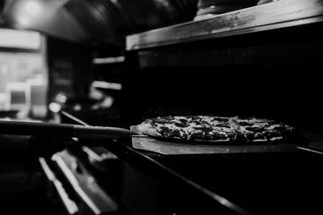 Fresh flatbread pizza being stone baked - pepperoni, cheese and tomato sauce in black and white