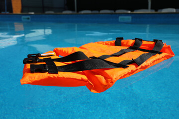 Bright orange life jacket floating in swimming pool