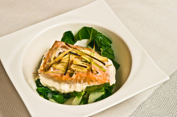top view, close distance of, a roasted, coconut salmon fillet, with roasted leeks and wilted Spinach, in a deep square, white bowl