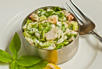 top view, close up of chopped shrimp. lettuce, salad in metal mold with an artisan fork on white, round plate
