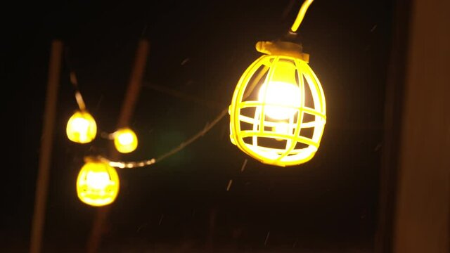 Slow motion tight shot of work light string swinging in snow storm