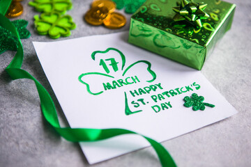 Decorative clover leaves, green gifts box, coins on stone background, flat lay. St. Patrick's Day...