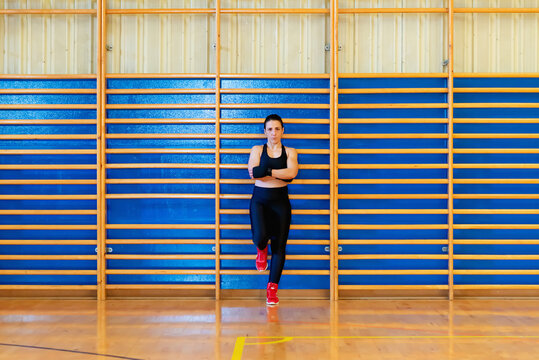 Female fighter leaning on wooden bars ladder at gym looking at camera