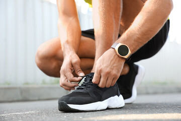 Obraz premium Man with fitness tracker tying shoelaces outdoors, closeup