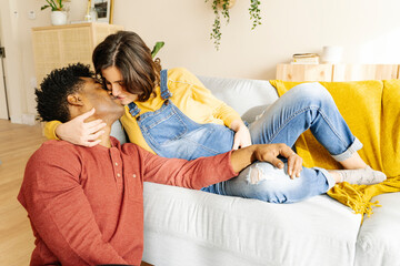 Husband kissing his pregnant wife on a sofa. Interracial couple concept