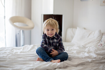 Cute toddler child sitting in the bed, smiling at camera