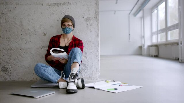 Student with face mask sitting on floor back at college or university, looking at camera. Coronavirus concept.