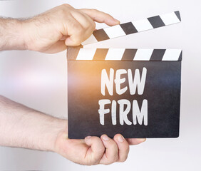 On a white background, a man holds a clapperboard in his hands on which it is written - NEW FIRM