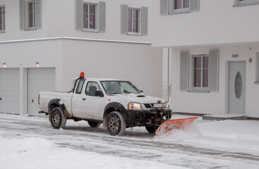 A pickup truck equipped with a plow is removing snow from a sloped driveway in winter. White pickup truck with plow. Clearing the streets from snow. © ibilyk13