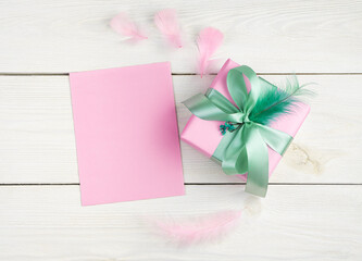 A pink envelope and a gift box with feathers on a light wooden background. Top view with copy space. Holiday background, March 8.