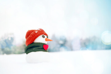 Little snowman in a orange cap and a green scarf with red heart on snow in the winter, closeup....
