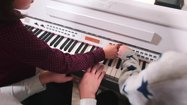 The hands of the students and the teacher play the piano keys in a music school. Improvisation of sounds when teaching. Spontaneous inspiration.
