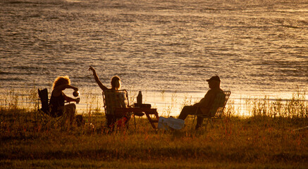 personas divirtiéndose y conversando a a la orilla de un lago durante un atardecer tranquilo de verano caluroso