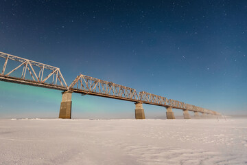 modern railway bridge in winter across the frozen northern river in the background northern lights