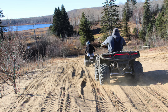 A young by and adult riding their atvs down a hill