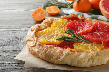 Delicious galette with citrus fruits and rosemary on wooden table, closeup