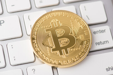 Close up top overhead view photo of golden bit coin laying on white buttons of laptop keyboard on the background