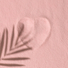 Palm shadow over heart sighn in pink gold sand. Abstract creative layout. Minimal concept. Celebration of love.