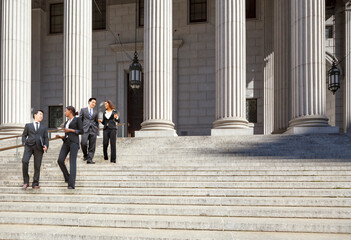 Four well dressed professionals walk down steps in discussion outside of a courthouse. Could be lawyers, business people etc. - obrazy, fototapety, plakaty