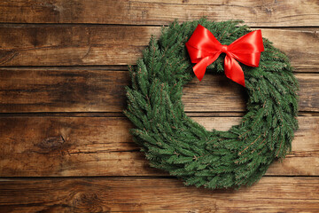 Christmas wreath made of fir branches with red bow on wooden background, top view. Space for text