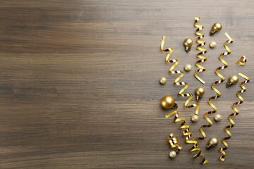 Shiny serpentine streamers and Christmas balls on wooden background, flat lay. Space for text