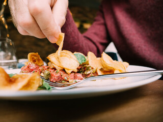 Close-up image of male hand eating from the plate potatoes chips with veal meat and salad - delicious meal in restaurant cafe