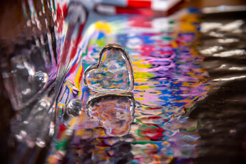 close up of glass heart on colorful ripples of water