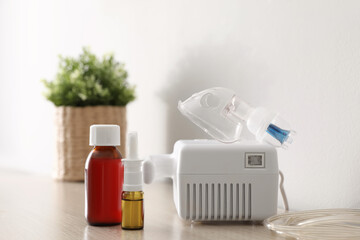Modern nebulizer with face mask and medications on wooden table indoors. Inhalation equipment
