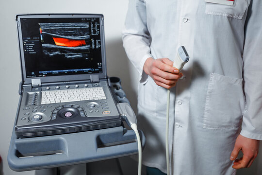 Doctor standing with apparatus for varicose laser treatment on female legs in clinic.
