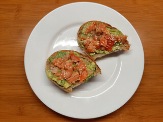 two sandwiches of white bread, avocado and red fish with sesame seeds are on a white plate