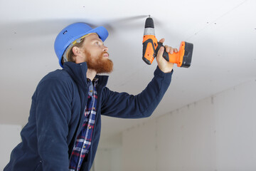 an electrician is drilling a ceiling with a perforator