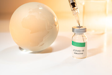 Glass globe and syringe with Covid-19 vaccine and beaker on white background . Global health care concept