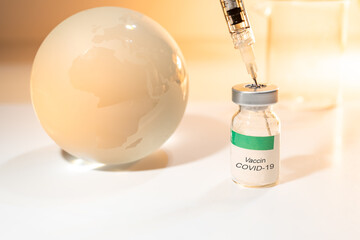 Glass globe and syringe with Covid-19 vaccine and beaker on white background . Global health care concept