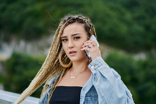 Close-up portrait of a young woman with braided blonde hair talking on her mobile phone