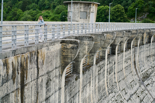Young woman with blonde braided hair wearing a denim jacket and white jean resting on a dam