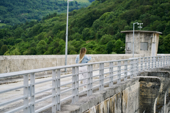 Young woman with blonde braided hair wearing a denim jacket and white jean resting on a dam