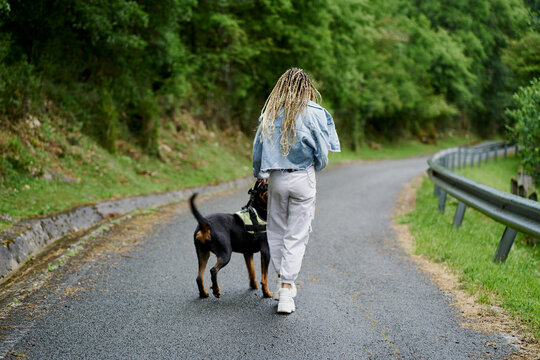 Young woman with blonde braided hair wearing a denim jacket and white jean walking her dog on a rainy day