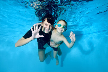 Portrait of a beautiful boy and his female coach underwater. They smile, look at the camera, and...