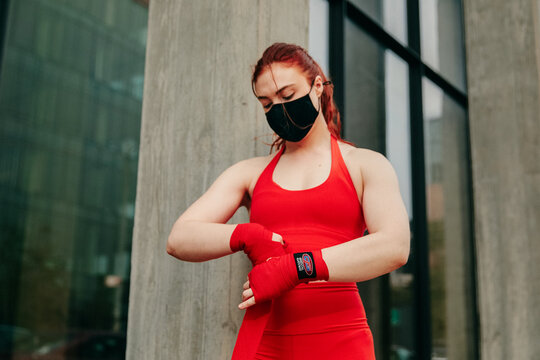 Young female boxer, wrapping wrist in Brooklyn street, with face mask.