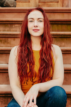Portrait of a young woman with red hair sitting outdoors on a stoop.