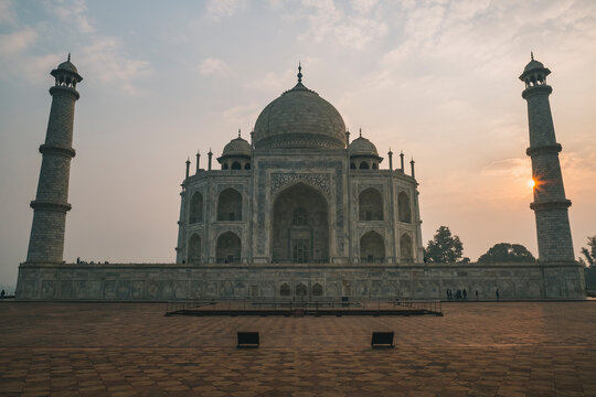 Taj Mahal west face against cloudy sky and sun peaking on one of the minarets, during sunrise time, Agra, India