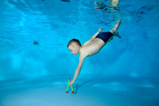 A picture of a sporty boy who dives to the bottom of the pool for a toy. Fun dives underwater. Active happy child. Swimming classes. Bodily exercises. Healthy lifestyle.