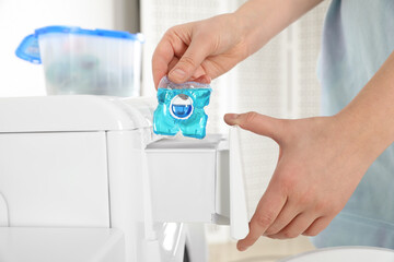 Woman putting laundry detergent capsule into washing machine, closeup